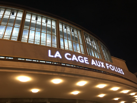 Beleuchteter Schriftzug „La Cage auf folles an der Berliner Komischen Oper bei Nacht mit Fenstern