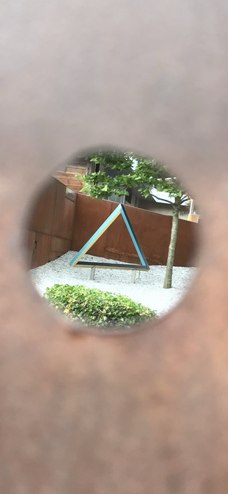 Blick durch ein Loch einer rostigen Metallplatte auf ein Dreieck