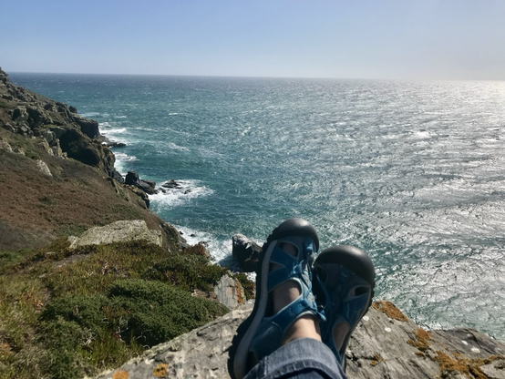 Sandalen im Vordergrund vor Blick über Steilwand und Meer (türkis-blau)