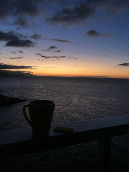 Im Vordergrund sieht man eine Teetasse im Dunkeln vor einem Sonnenuntergang über dem Meer