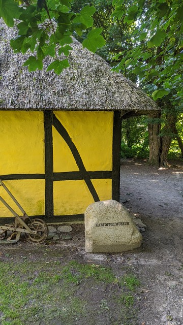 Eingang zum Museum. Ein Reed gedecktes, gelbes Haus mit Fachwerk. Davor ein großer Stein mit der Aufschrift: Kartoffelmuseum (sic)