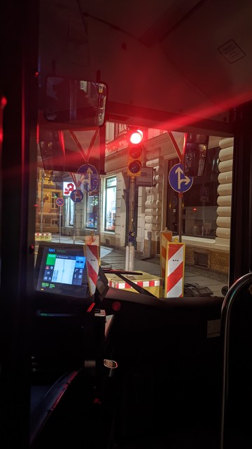 Ich sitze bei dem Bild direkt hinter der Fahrenden und fotografierte nach rechts vorn während der Bus an einer roten Ampel hält. Reflektionen in der Scheibe zwischen dem Fahrerbereich und dem Fahrgastraum von den Geschäften an der Kreuzung, die Baken und dem Bildschirm der Fahrdenden. Alles statisch und ruhig.

Sehr schwere Beschreibung, aber gut es zu tun. LG