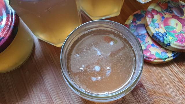 Marmeladenglas von oben hineinfotgrafiert. Weiss-gelbe Füllung. Daneben ein paar Deckel mit Obstmuster und weitere Gläser, die bereits zugeschraubt sind.