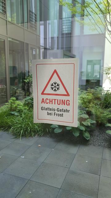 An einer Glastür zu einem Innenhof hängt ein Schild mit der Aufschrift "Achtung - Glatteis-Gefahr bei Frost"