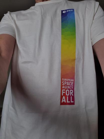 Selfie mit einem T-Shirt der ESA. Auf der linken Seite des Shirts ist ein Streifen mit Regenbogenmuster und dem Text "European Space Agency For All"