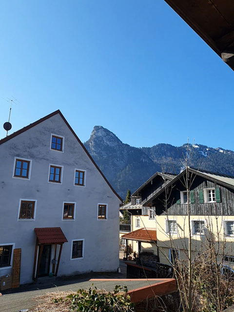 Auf dem Video ist links im Bild eine Hausfassade zu sehen. Hinter dem Haus erhebt sich der Kofel, rechts ein weiteres Haus, aus dessen Schornstein ein bisschen Rauch aufsteigt