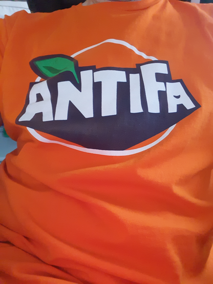 Orangenes Shirt mit einem Aufdruck. Auf den ersten Blick wie das Fanta Logo. Text ist allerdings "Antifa" mit einem kleinen grünen Blatt quer über dem N