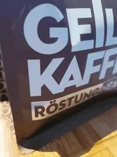 GIF, das zuerst die Vorderseite einer Kaffeepackung zeigt. Diese ist braun mit weiß/silbernem Schriftzug. Dann kippt die Packung nach hinten und auf dem Boden steht in einem weissen Kreis der Name des Herstellers 'Geiler Kaffee'. Links und rechts davon ziehen sich die Pride Farben als Streifen que(e)r über den Boden
