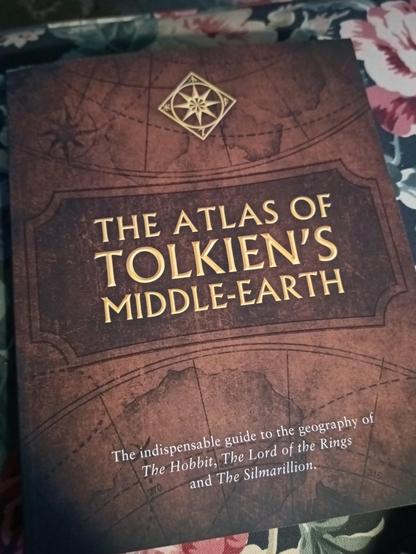 Bild der Vorderseite eines Atlanten. Auf dem in braun gehaltenen Hintergrund steht in goldfarbener Schrift "The Atlas Of Tolkien's Middle-Earth"
Darunter in kleinerer Schrift "The indispensible guide to the geography of The Hobbit, The Lord of the Rings and The Silmarillion"